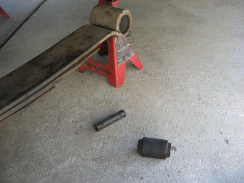 1994 Ford Bronco - Leaf spring and bushings are shown on a concrete surface, supported by a red jack stand.