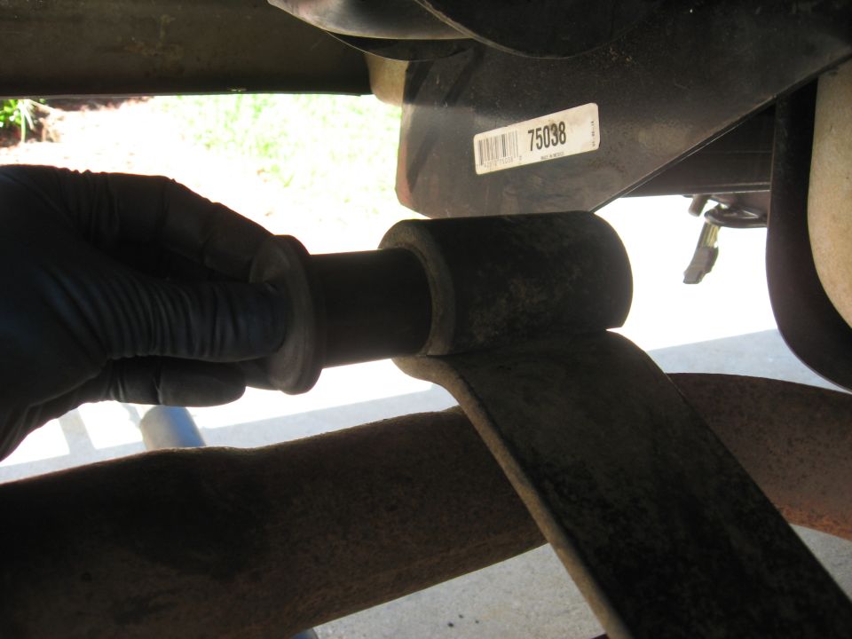 Gloved hand installing a leaf spring bushing on a vehicle's suspension