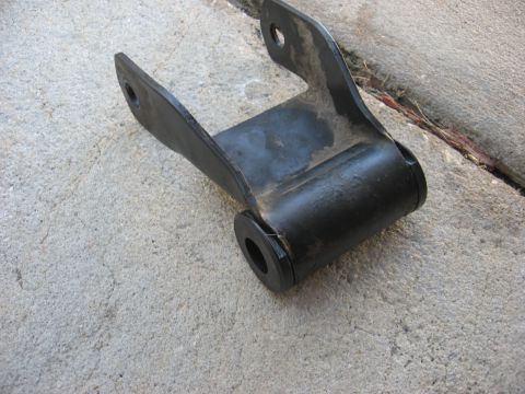 1994 Ford Bronco - A black metal leaf spring shackle with rubber bushings is shown on a concrete surface.