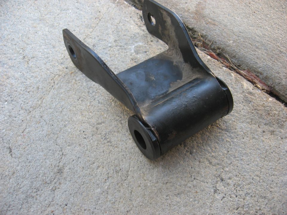 Black metal leaf spring shackle with rubber bushings, resting on concrete