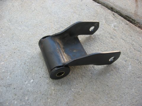 1994 Ford Bronco - A black metal leaf spring shackle with a rubber bushing sits on a concrete surface.