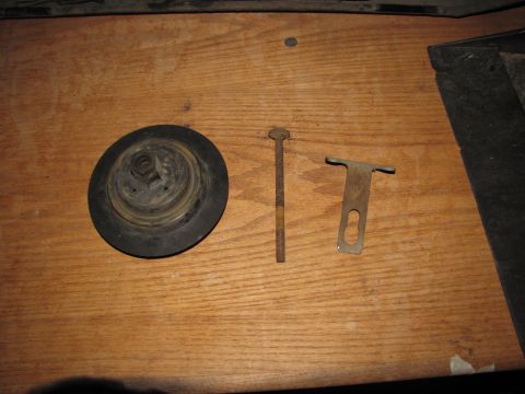 1992 Ford F-150 - Three assorted automotive parts, including a round rubber component, a bolt, and a metal bracket, are laid out on a wooden surface.