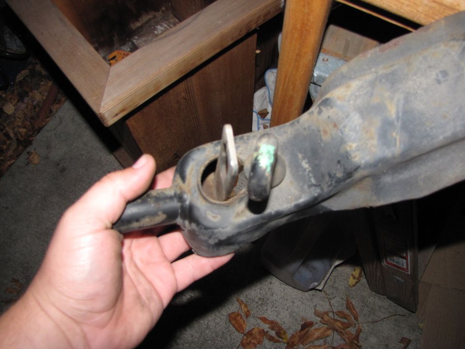 Hand holding a black metal vehicle suspension part with a metal pin inserted into a hole
