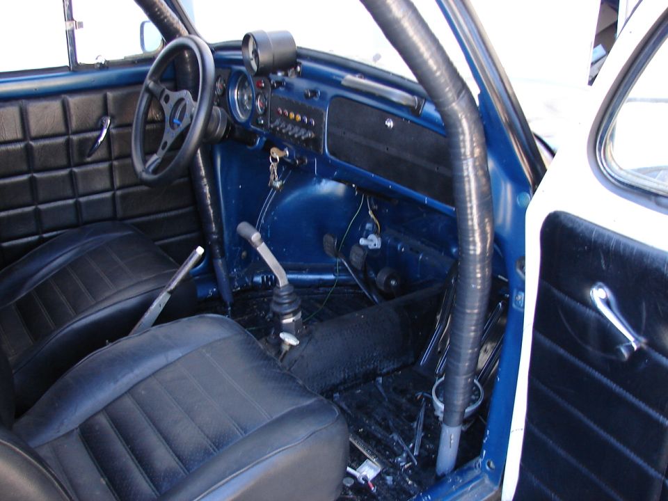 Interior of a blue Volkswagen Beetle with black seats, roll cage, and aftermarket gauges