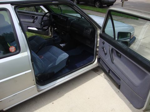 1985 Volkswagen GTI - The interior of a silver Volkswagen Golf shows blue fabric seats and door panels with the doors open.