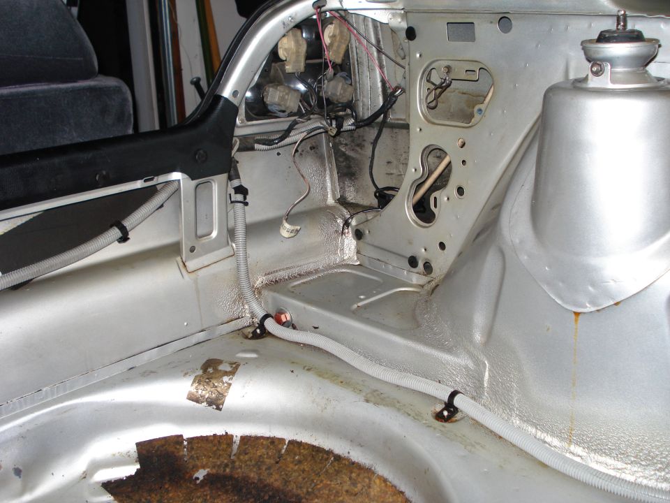 Disassembled car interior showing bare metal floor, wiring, and suspension mount