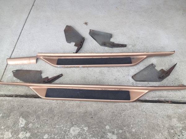 pair of bronze running boards with black grip tape and several metal brackets