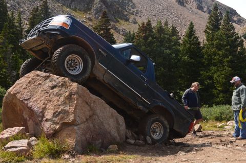 1983 Ford Bronco - A dark blue Ford Bronco navigates a rocky trail, with two men observing the action.