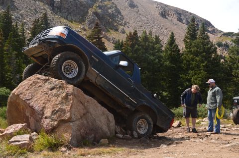 1983 Ford Bronco - A dark blue Ford Bronco navigates a challenging rock obstacle on an off-road trail.
