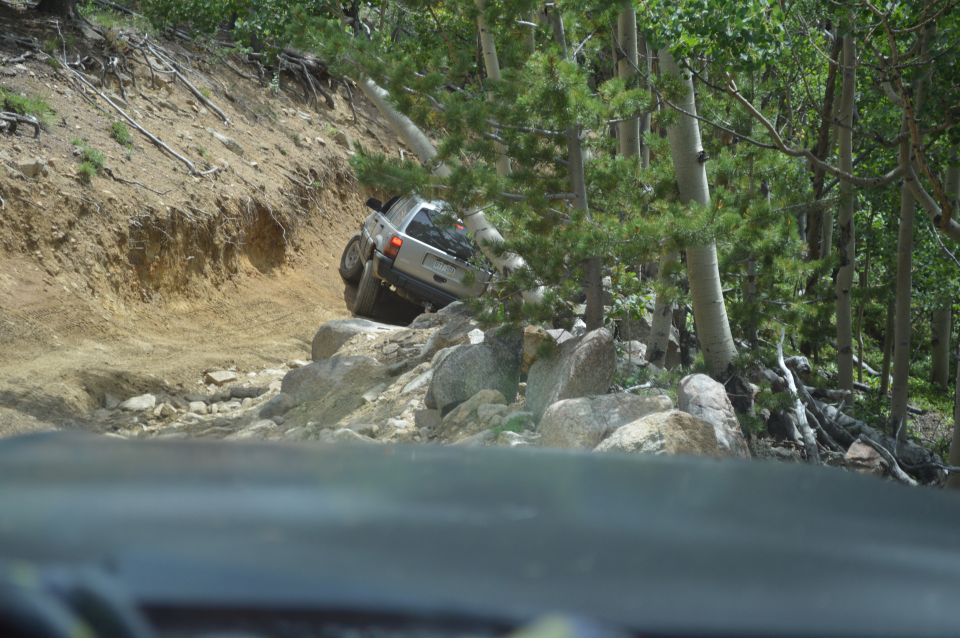 Silver SUV navigating a steep, rocky off-road trail with trees and dirt embankment