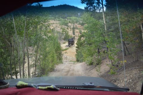 1983 Ford Bronco - Driving on a dirt road towards a mine structure, surrounded by trees and a mountain landscape.