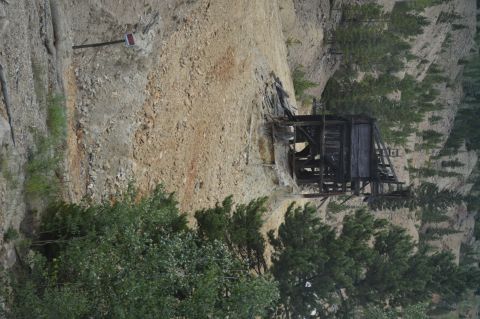 1983 Ford Bronco - An old wooden structure sits on a steep, rocky slope surrounded by trees.