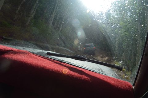 1983 Ford Bronco - Two vehicles navigate a challenging muddy path through a dense forest.
