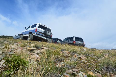 1983 Ford Bronco - Several SUVs are parked on a rocky hill under a cloudy sky.