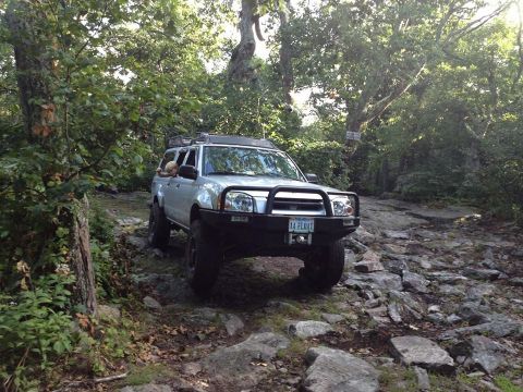2003 Nissan Frontier - This modified 2003 Nissan Frontier navigates a challenging rocky path through a wooded area.