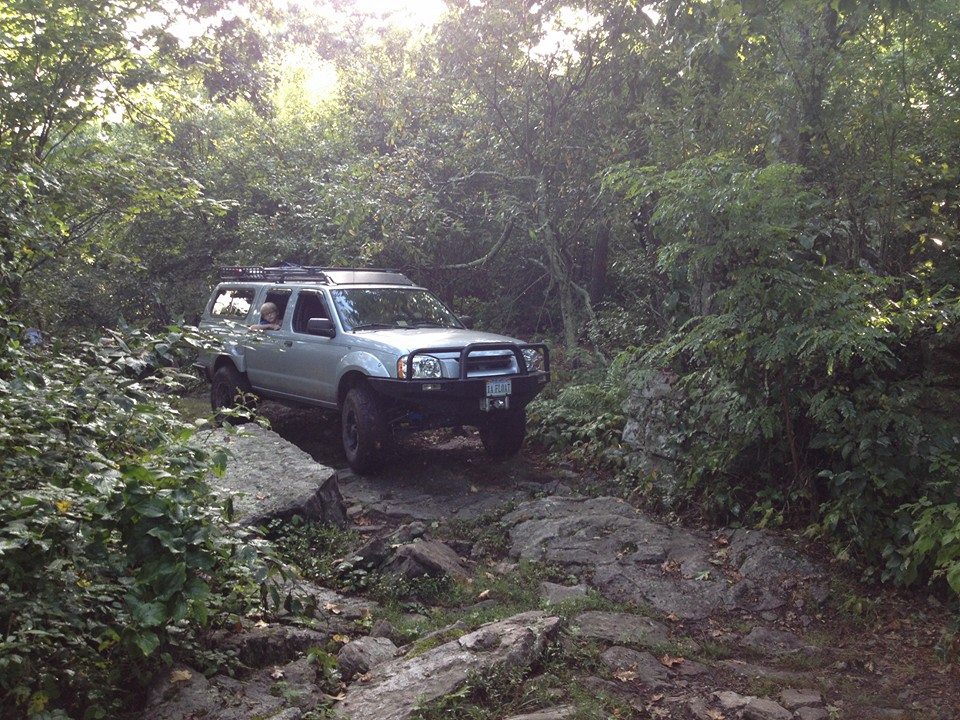 Silver Nissan Frontier driving on a rocky trail through trees