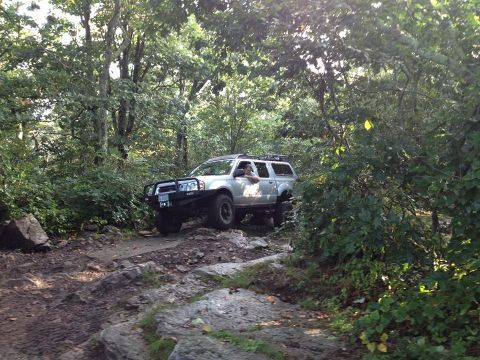 2003 Nissan Frontier - A 2003 Nissan Frontier navigates a challenging off-road path surrounded by dense forest foliage.