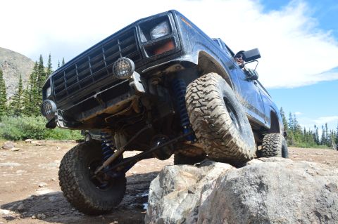 1983 Ford Bronco - An off-road SUV navigates a rocky terrain under a bright blue sky.