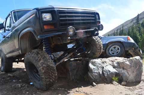 1983 Ford Bronco - Two off-road vehicles navigate a rocky obstacle on a mountain trail.