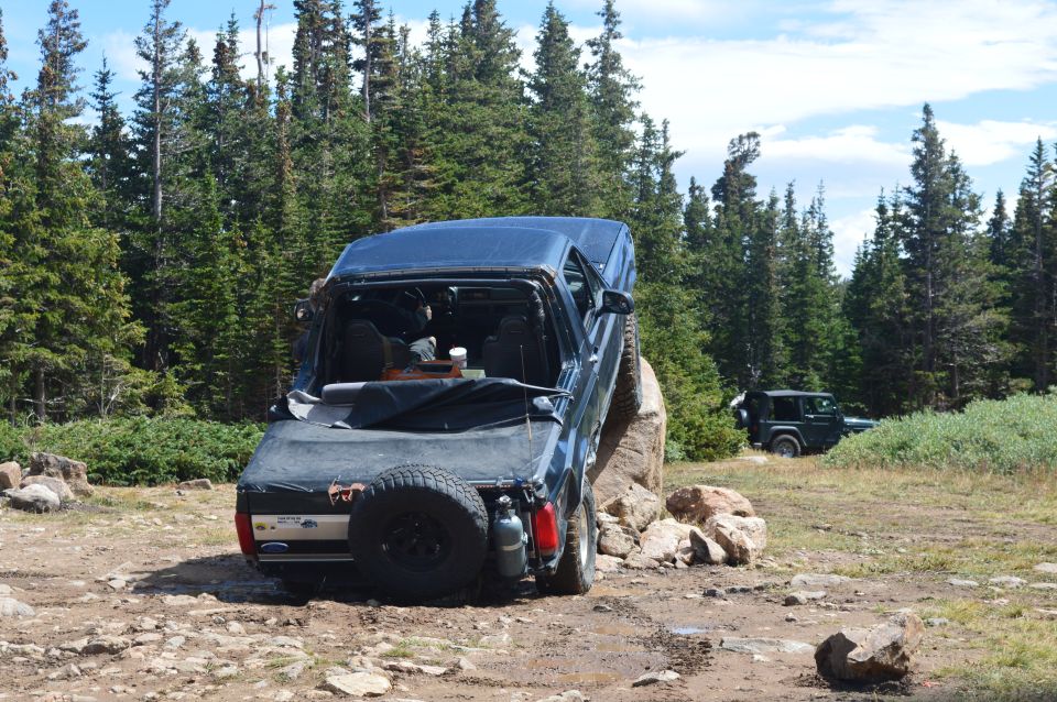Dark blue SUV with a soft top, rear view, driving over a large rock