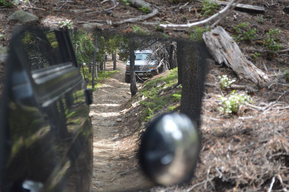 View from inside a vehicle looking out at another Bronco on a dirt trail in the woods