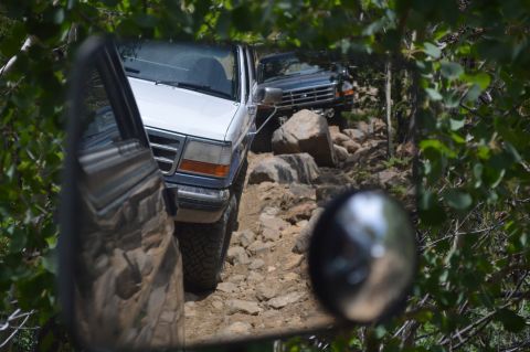 1983 Ford Bronco - Two Ford Broncos navigate a rocky trail, with the front vehicle in white and the rear in dark blue.