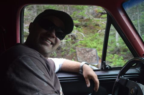 1983 Ford Bronco - A man is seen from the chest up, smiling while sitting in the driver's seat of a vehicle.