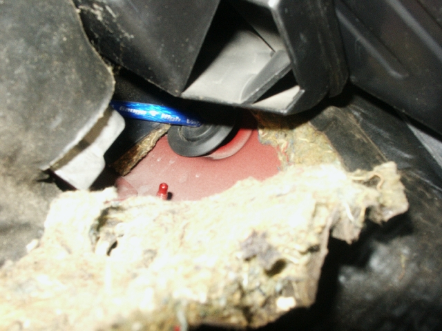 Close-up of frayed insulation and wiring under a car's dashboard, with a blue light visible