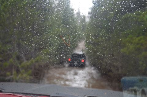 1983 Ford Bronco - Driving through a muddy trail with another vehicle ahead, seen through a rain-covered windshield.