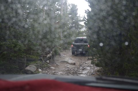 1983 Ford Bronco - A pickup truck navigates a challenging, wet forest road, with raindrops distorting the view from the driver's perspective.