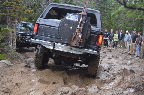 1983 Ford Bronco - A group of people watch as a black Ford Bronco navigates a challenging off-road course.