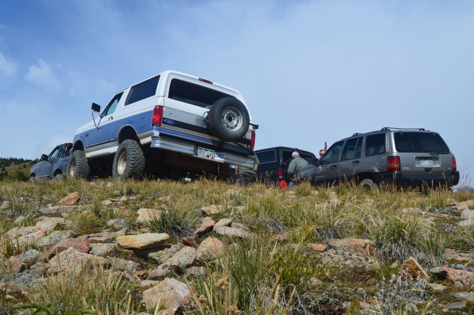 1992 Ford Bronco with spare tire on back, parked on rocks next to a Jeep Grand Cherokee