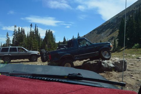 1983 Ford Bronco - Two SUVs traverse a challenging rocky path on a mountain trail under a clear blue sky.