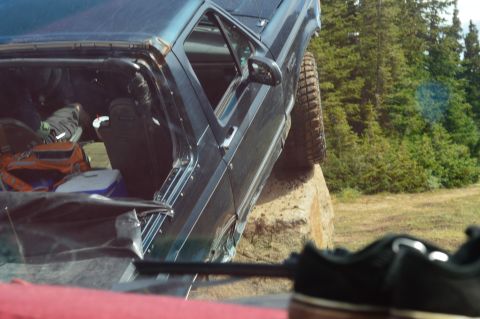1983 Ford Bronco - A dark blue SUV is precariously balanced on a large rock, with its interior filled with gear.
