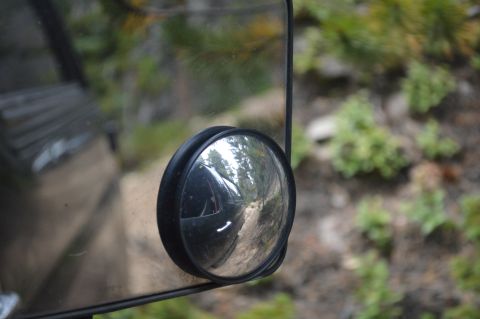 1983 Ford Bronco - Reflection in the side mirror shows a dirt road and trees, with the vehicle's side panel visible.