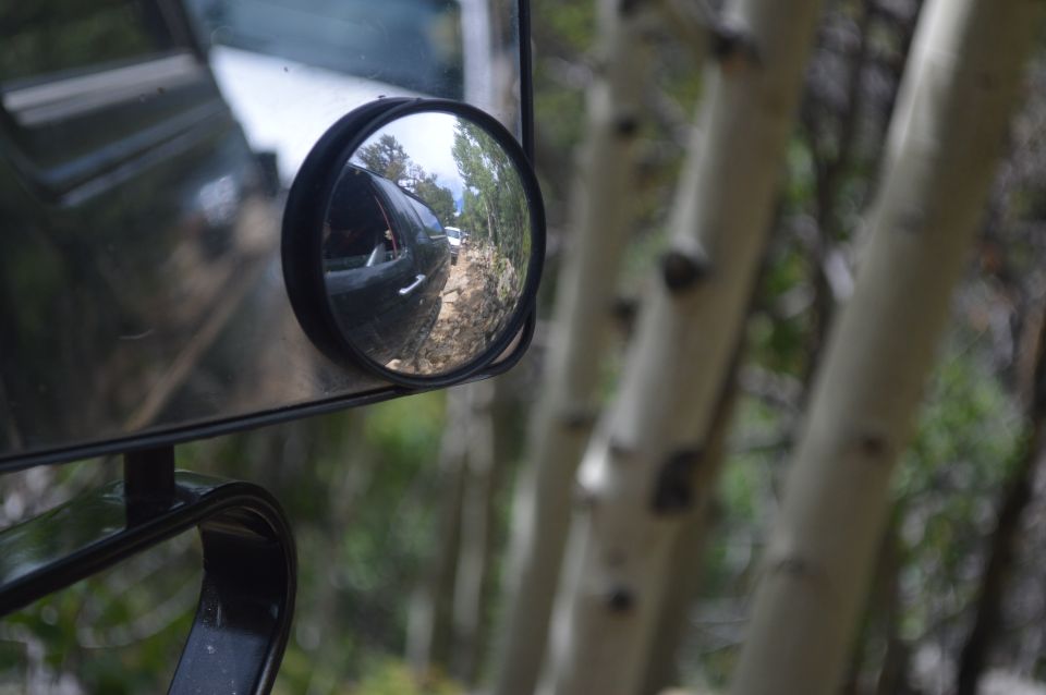 Side mirror reflection of dark SUV on dirt road with trees