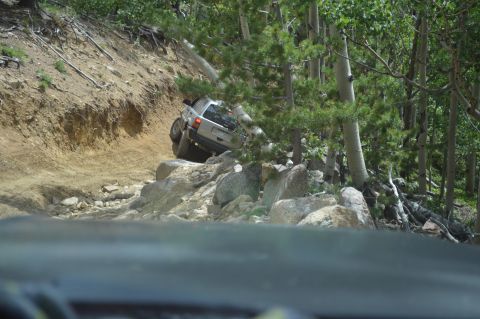 1983 Ford Bronco - A silver SUV is shown attempting to traverse a difficult, off-road path with large rocks and steep inclines.