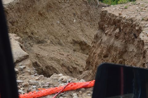 1983 Ford Bronco - View from a vehicle's side mirror shows a large dirt embankment and a collapsed road, with orange safety netting visible.
