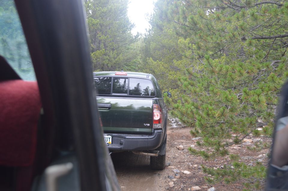 Dark green pickup truck driving on a dirt road through a forest. View from inside another vehicle