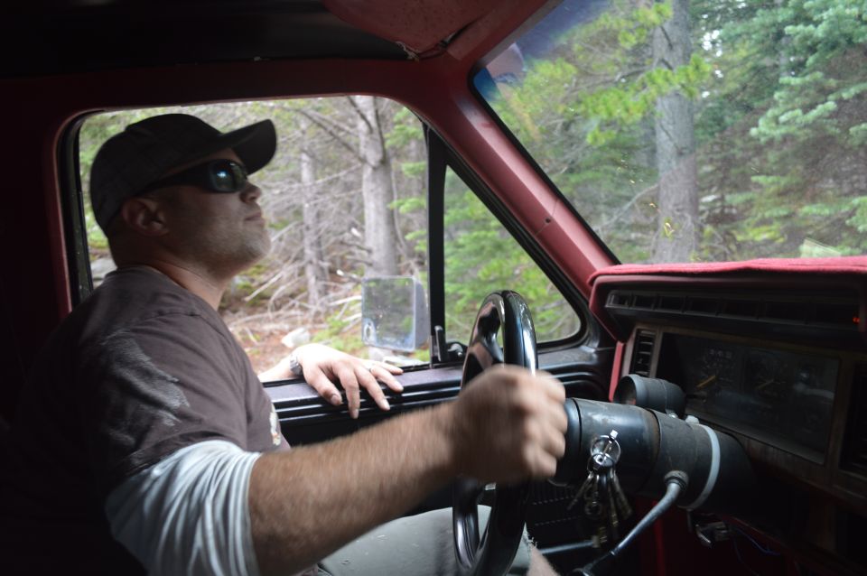 Man wearing a cap and sunglasses drives a truck through a wooded area