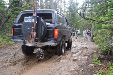 1983 Ford Bronco - Ford Bronco tackles a challenging muddy trail in a wooded area with a group of onlookers.