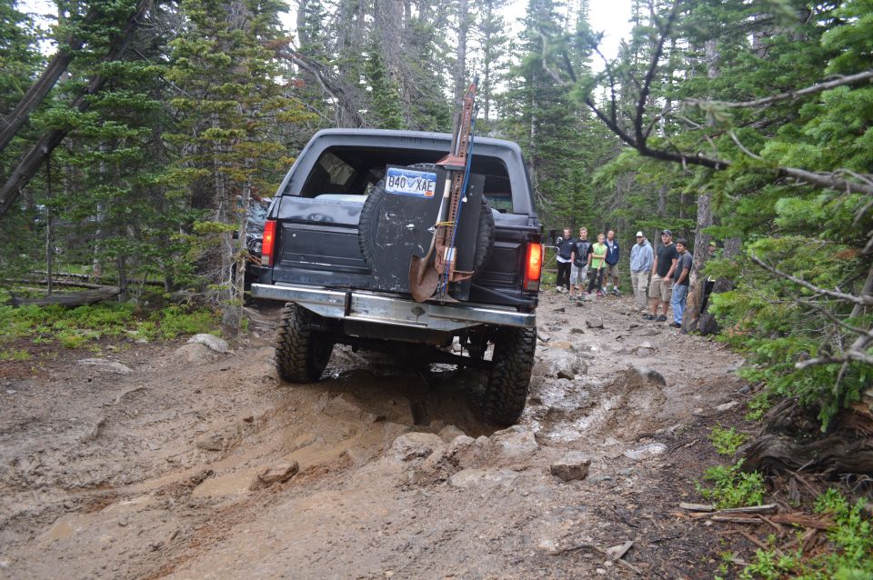 Black Ford Bronco on a muddy, rocky trail with a shovel and jack mounted on the spare tire