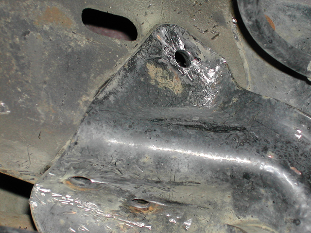 Close-up of a scraped metal underbody bracket with a bolt hole under a 1996 Ford Bronco