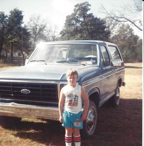 1982 Ford Bronco - A young boy poses in front of a blue Ford Bronco, likely from the early 1980s.
