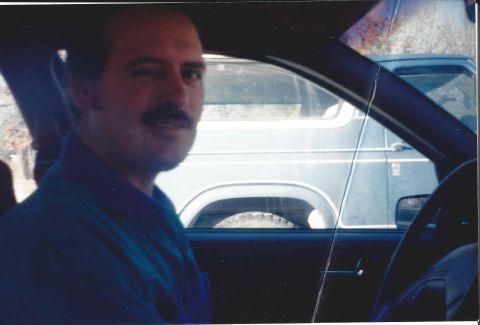 1982 Ford Bronco - A man winks at the camera from the driver's seat of a car, with another vehicle in the background.