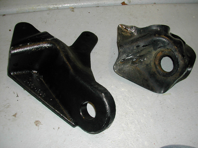 Two black metal mounting brackets on a concrete floor, one freshly painted, one dented and worn