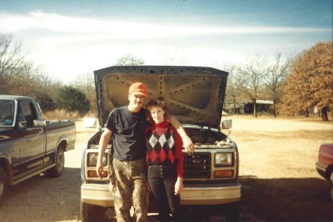 1982 Ford Bronco - Couple poses in front of a pickup truck, with another truck visible to the side.
