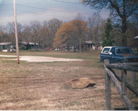 1982 Ford Bronco - A blue and white Ford Bronco is parked in a rural setting with houses and trees visible.
