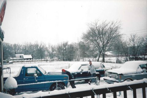 1982 Ford Bronco - Several vehicles are parked outside and covered in snow, with two people standing near one of them.