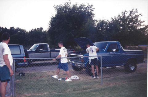 1982 Ford Bronco - Two men attend to a blue pickup truck with its hood open, while another truck waits nearby.